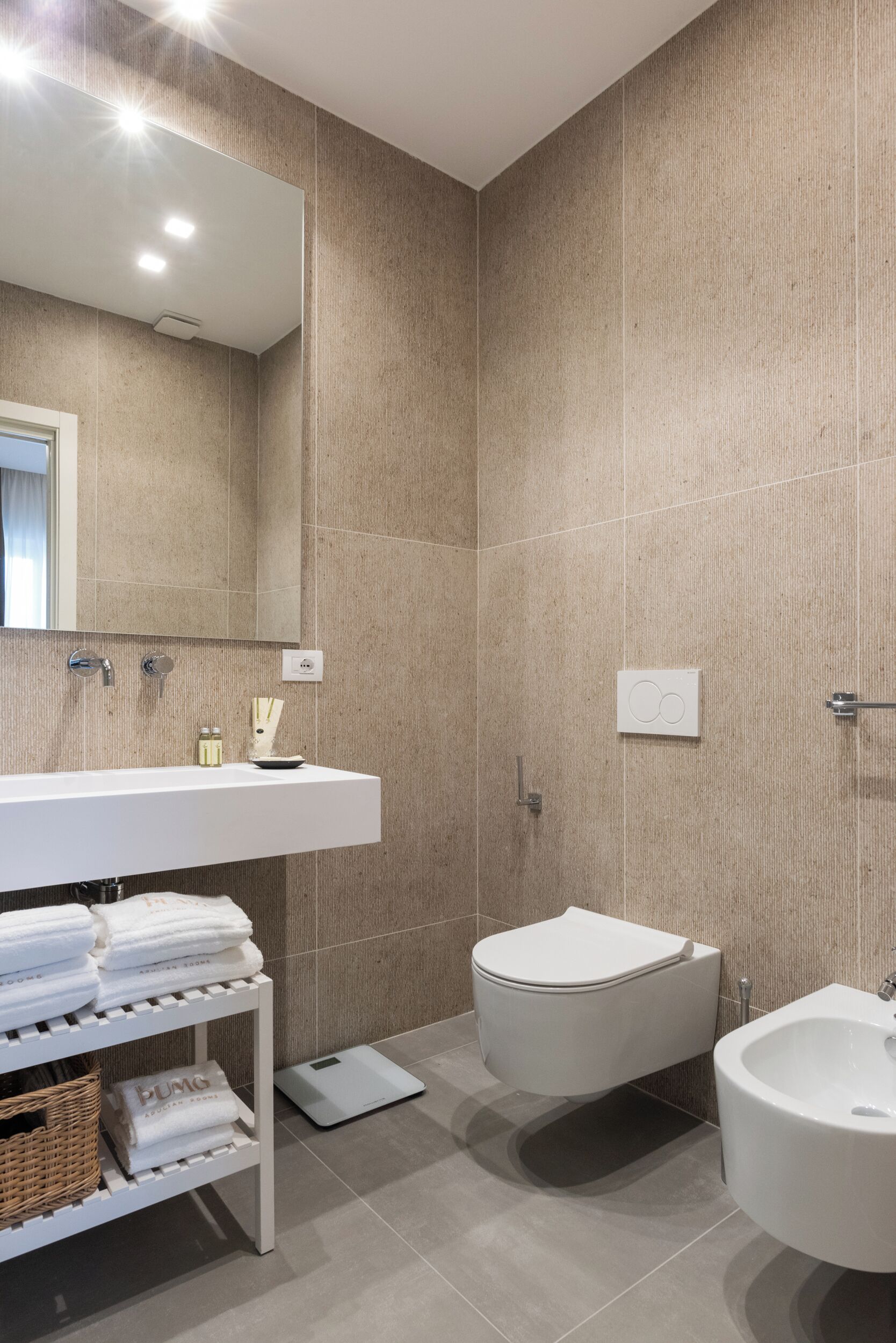 Un baño moderno con un tocador blanco, un inodoro, un bidé y un espejo grande.