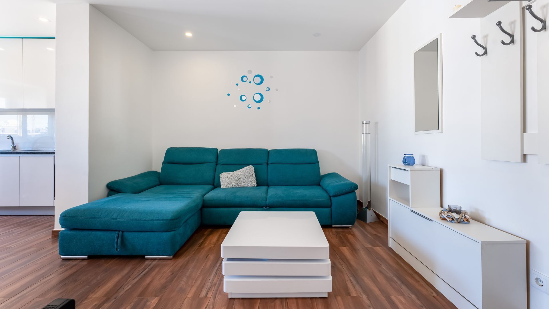 A modern living room with a teal sectional sofa, a white coffee table, and a minimalist decor.
