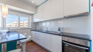Cozinha moderna com armários brancos, bancada preta, forno embutido e janela com vista para a cidade.