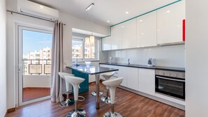 Cozinha moderna com ilha central, armários brancos e eletrodomésticos de aço inoxidável.