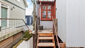 Una escalera exterior estrecha que lleva a una terraza de madera con una planta en maceta y una olla grande.