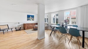 Un espacio habitable amplio con piso de madera, un sofá marrón, una mesa de comedor con sillas y un ventanal con cortinas.