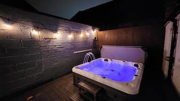 Un bain à remous doté d’une terrasse en bois et de murs en briques, le tout illuminé par des guirlandes lumineuses.