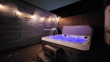 Ein Whirlpool mit einer Holzbank und Stufen, umgeben von einer Ziegelmauer und Lichterketten.