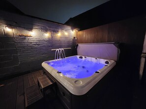 Un jacuzzi con un banco de madera y una pared de piedra con luces.