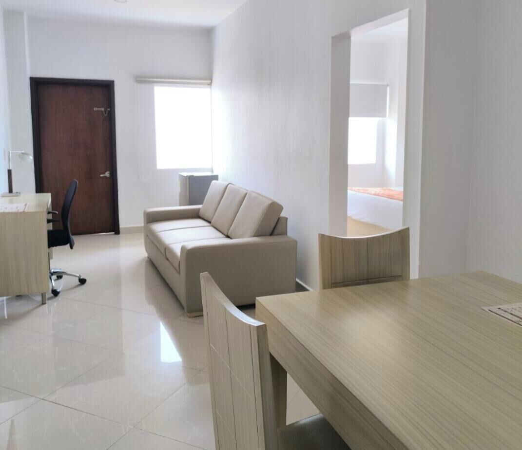 Ein modernes, helles Zimmer mit einer beigefarbenen Couch, einem Holzesstisch und einer kleinen Arbeitsnische mit Schreibtisch und Stuhl.