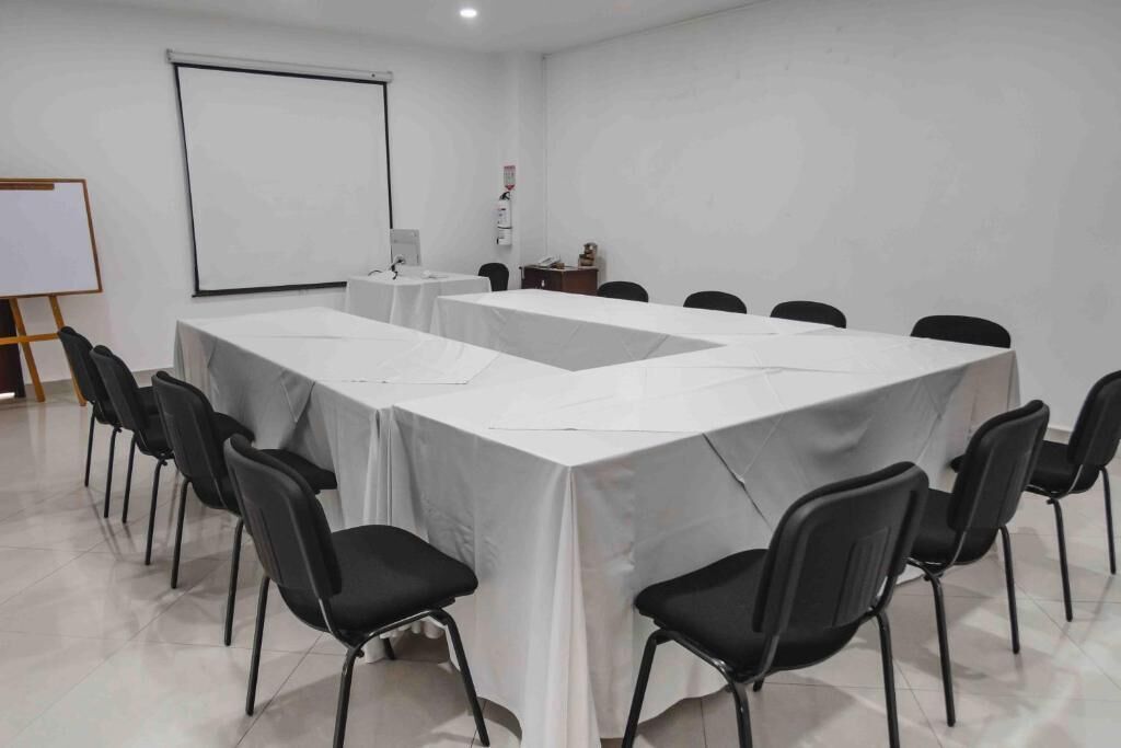A conference room with a long table, black chairs, a whiteboard, and a projector screen.