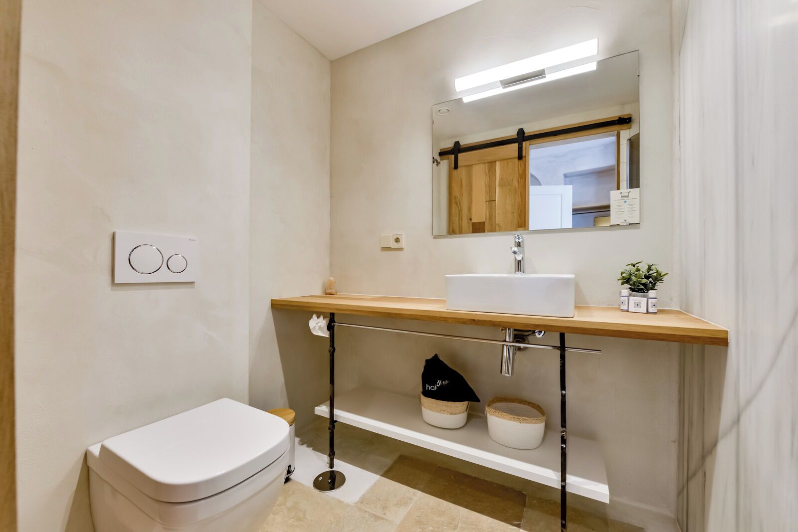 A modern bathroom with a white toilet, a wooden vanity with a white sink, a mirror, and a towel rack.
