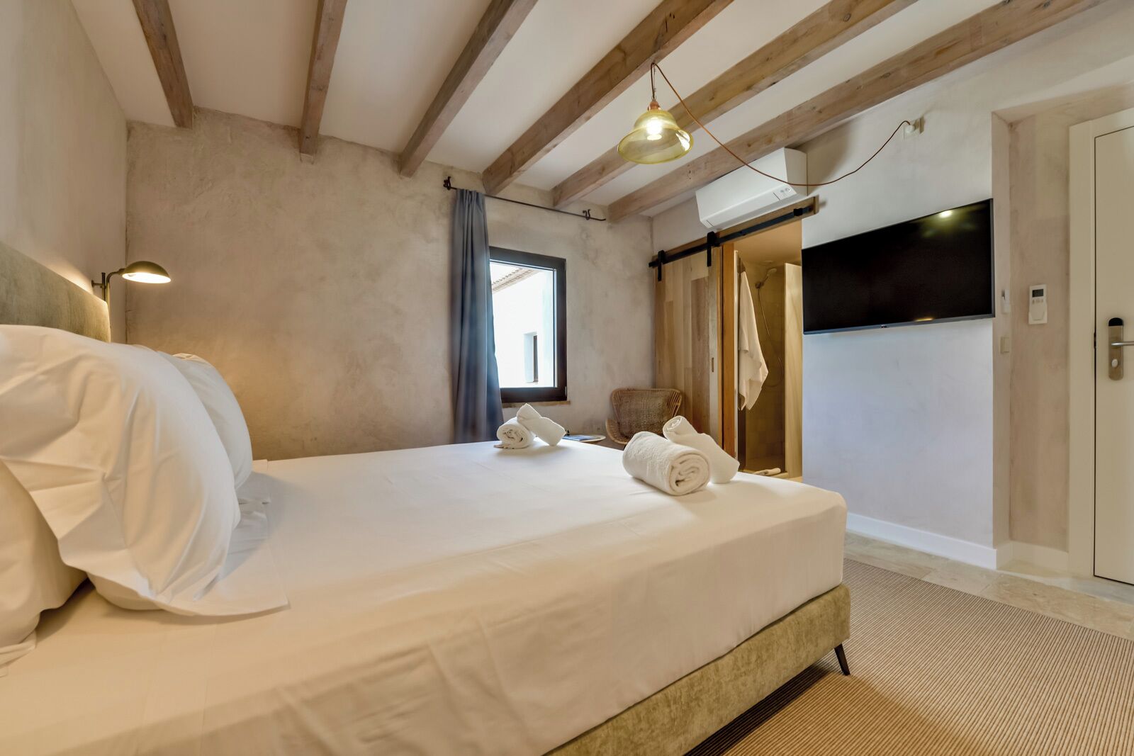 A bedroom with a bed, a window, a door, and a hanging light fixture.
