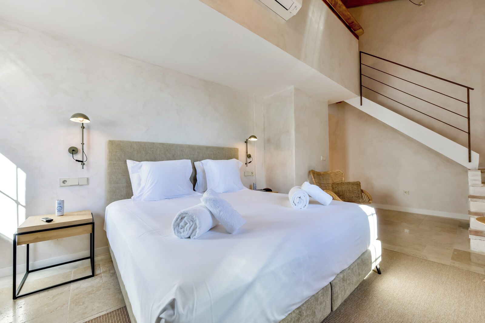 Un dormitorio espacioso con una cama grande, dos mesitas de noche, una lámpara de pared y una escalera.
