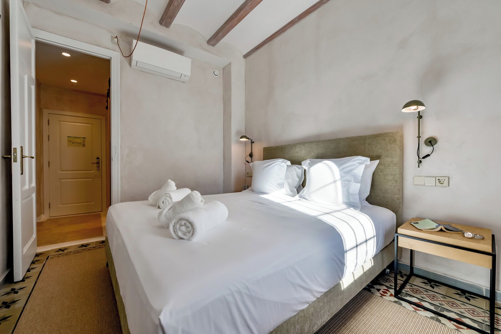 Hotelkamer met een bed, nachtkastje, lamp en deur naar een andere kamer.