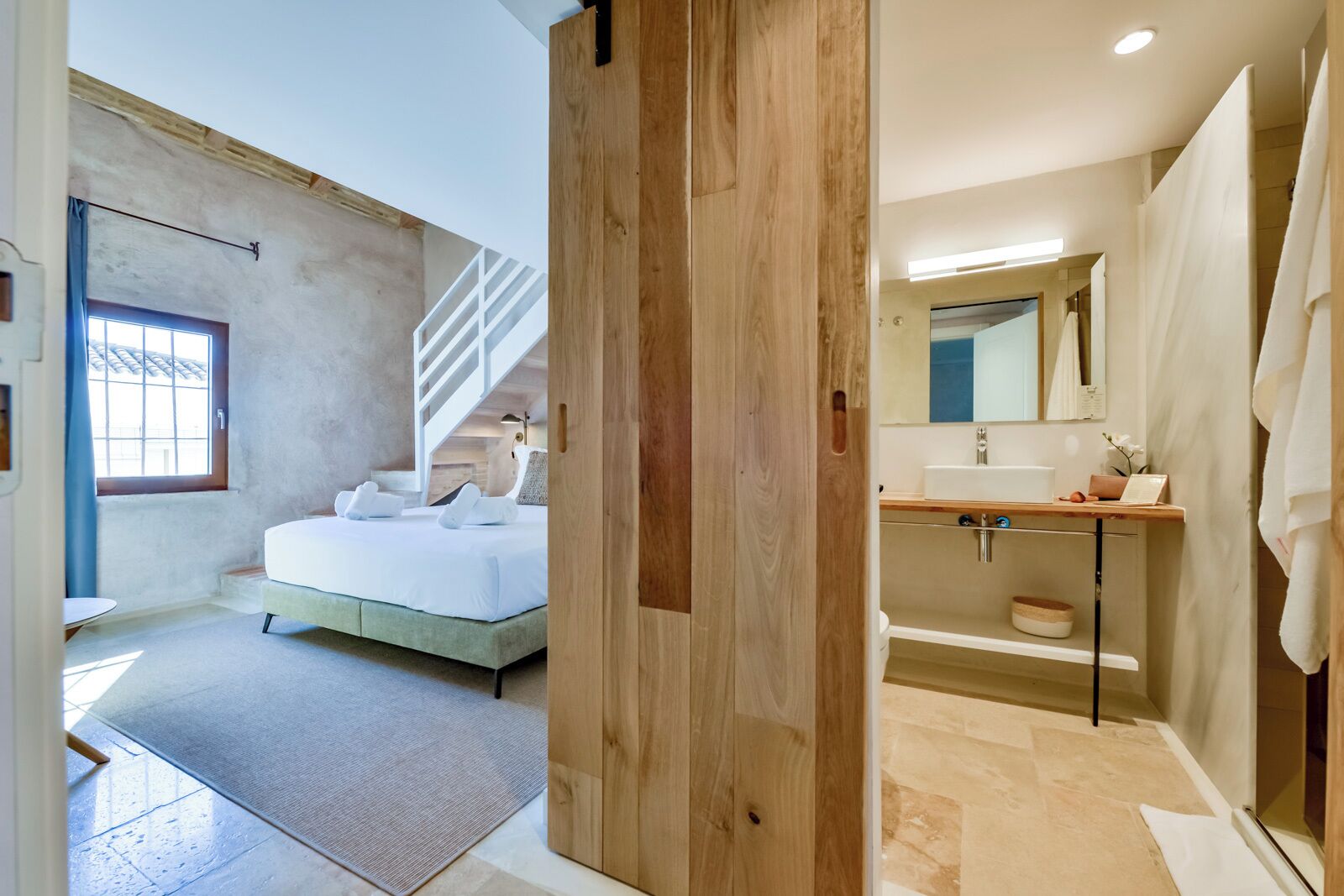 Un dormitorio moderno con una cama, una escalera y un baño con un lavabo y espejo.