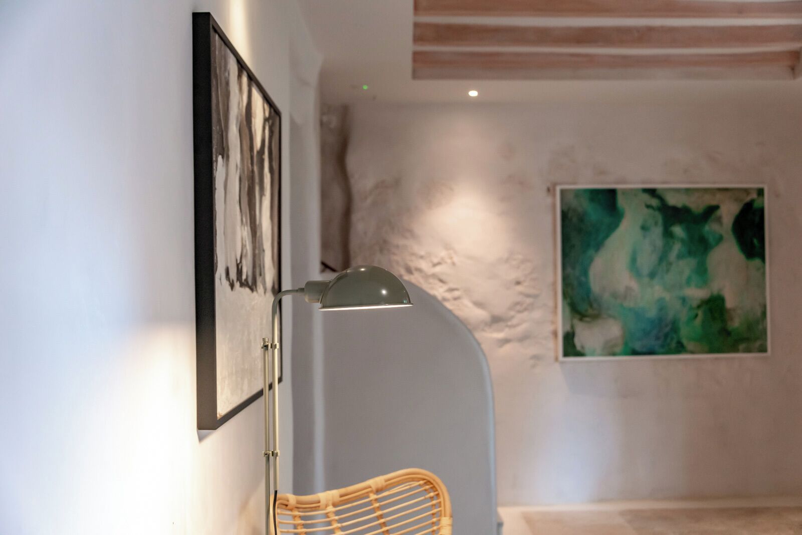 A modern interior with a wall-mounted lamp, a framed abstract painting, and a large abstract artwork on the wall.
