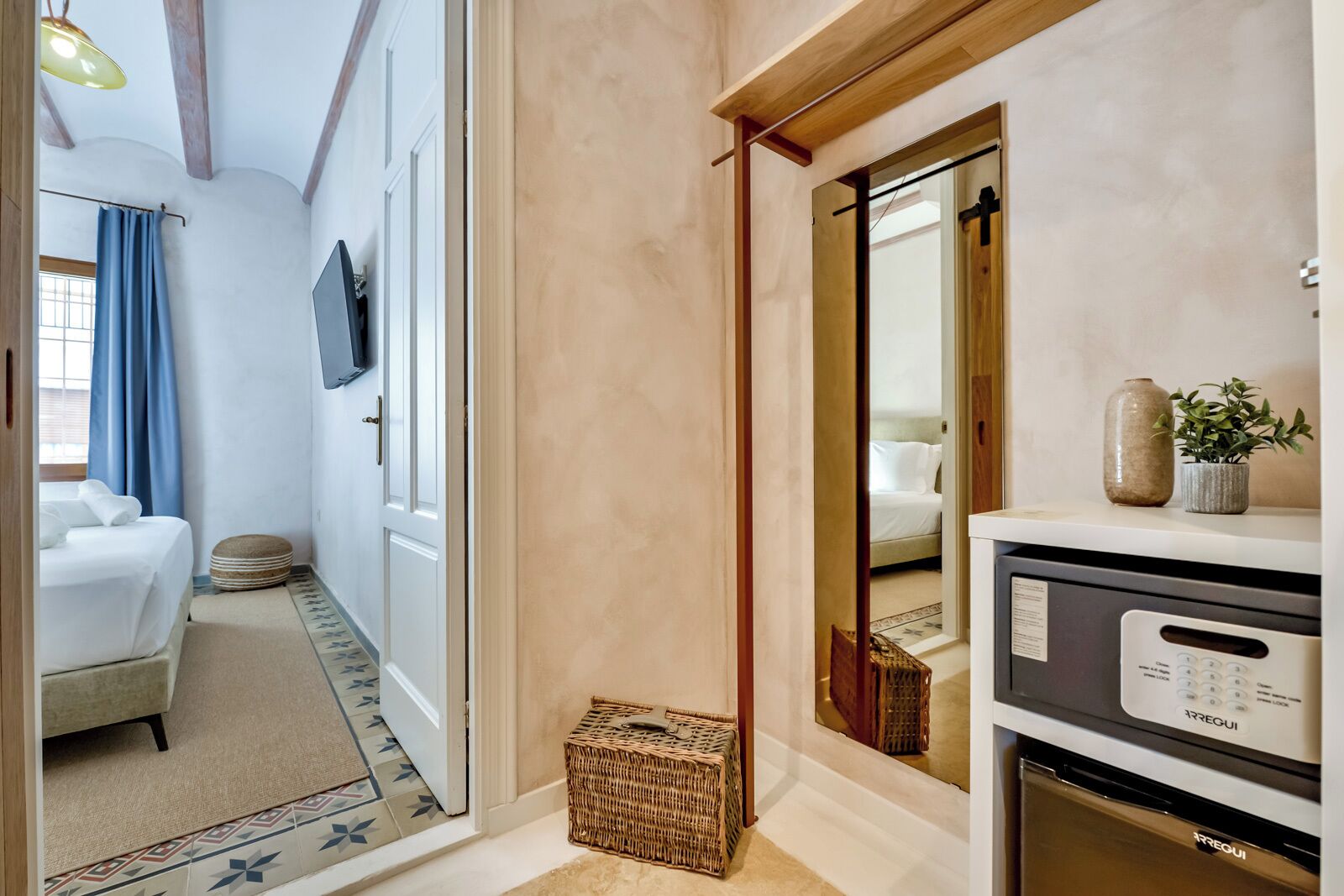 A hotel room with a bed, a TV, a mirror, a small table, and a dishwasher.