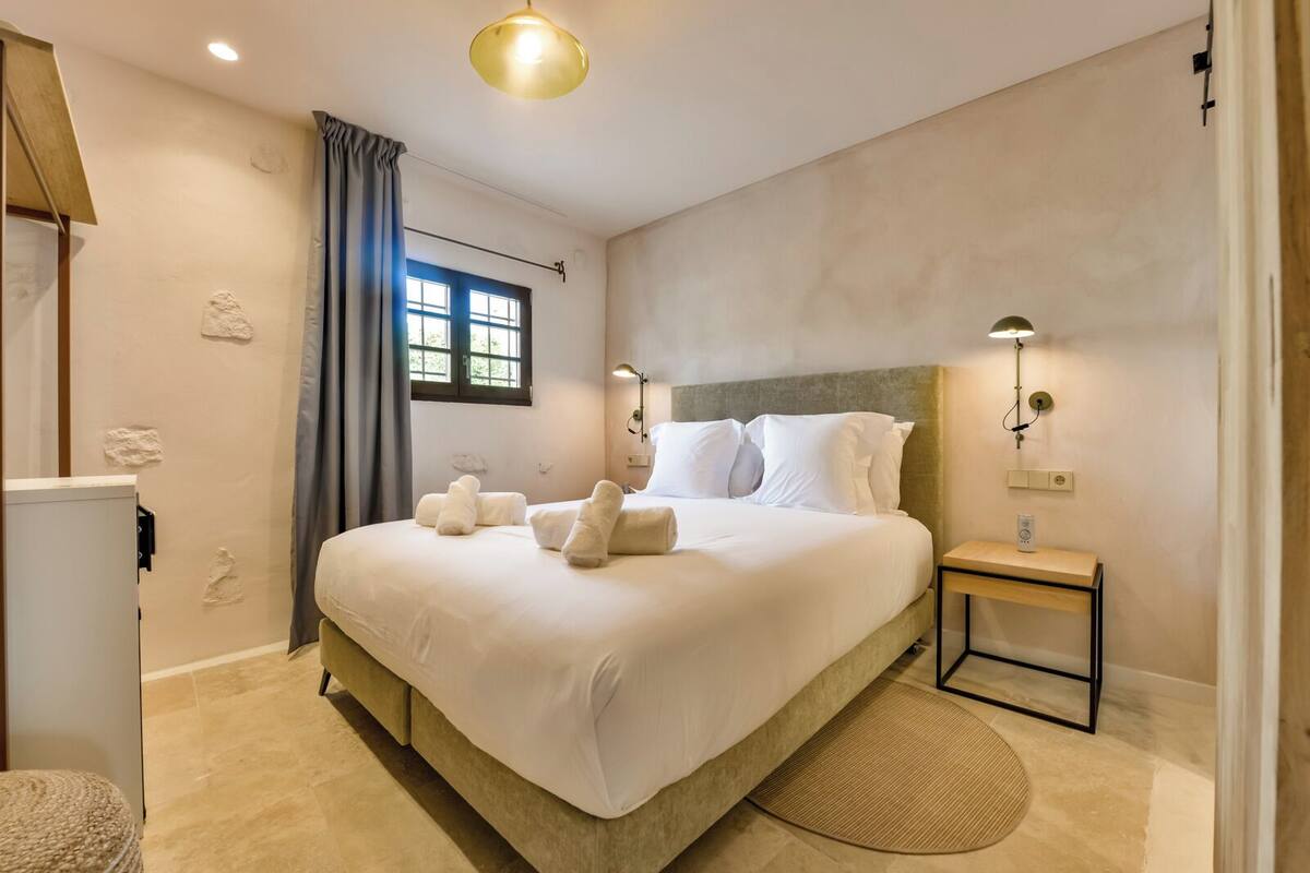 Une chambre d’hôtel avec un grand lit, une table de chevet, une lampe et une fenêtre avec des rideaux.