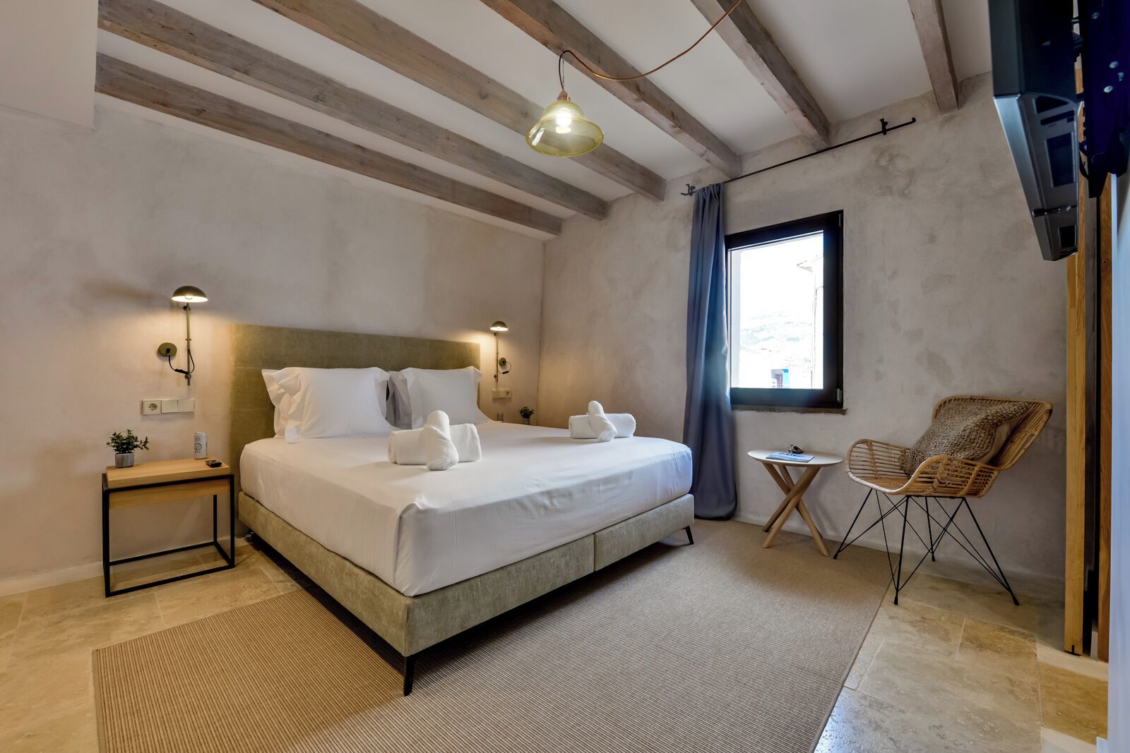Un dormitorio con una cama, mesitas de noche, una silla y una ventana.