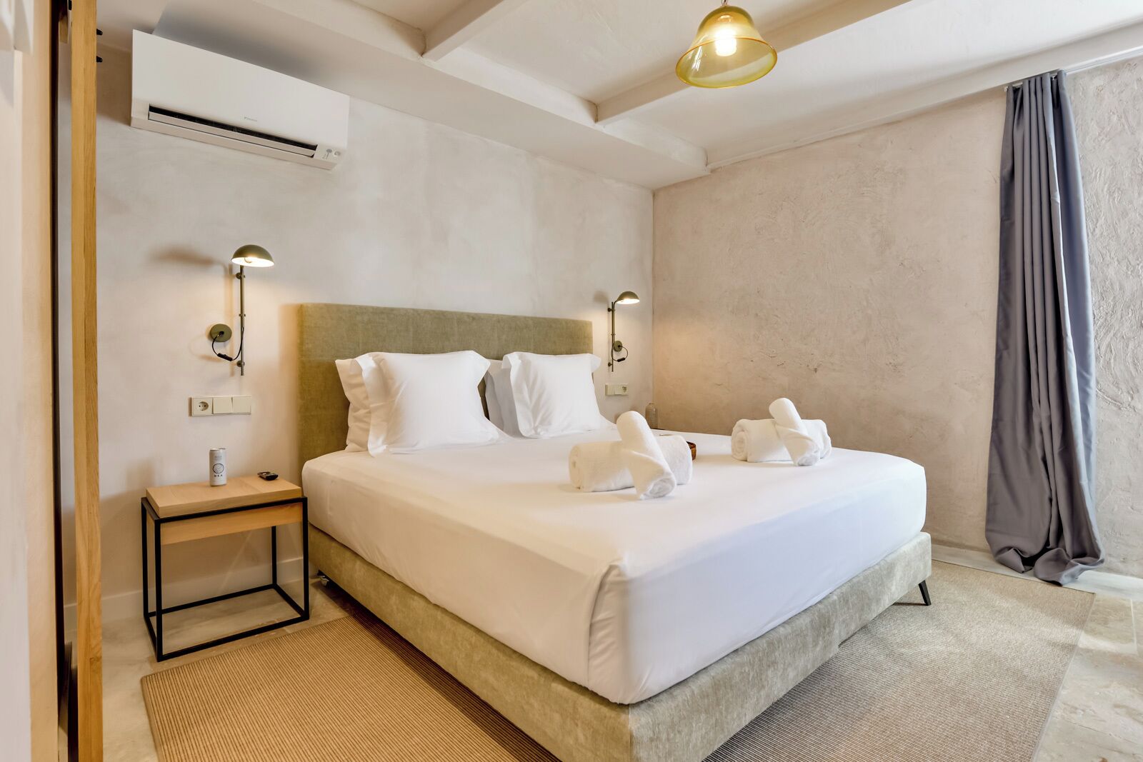 Habitación de hotel con una cama grande, dos mesitas de noche, aire acondicionado de pared y una lámpara en el techo.