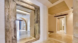 Un couloir doté d’un grand miroir qui reflète un intérieur moderne, avec des murs en pierre et un sol carrelé.