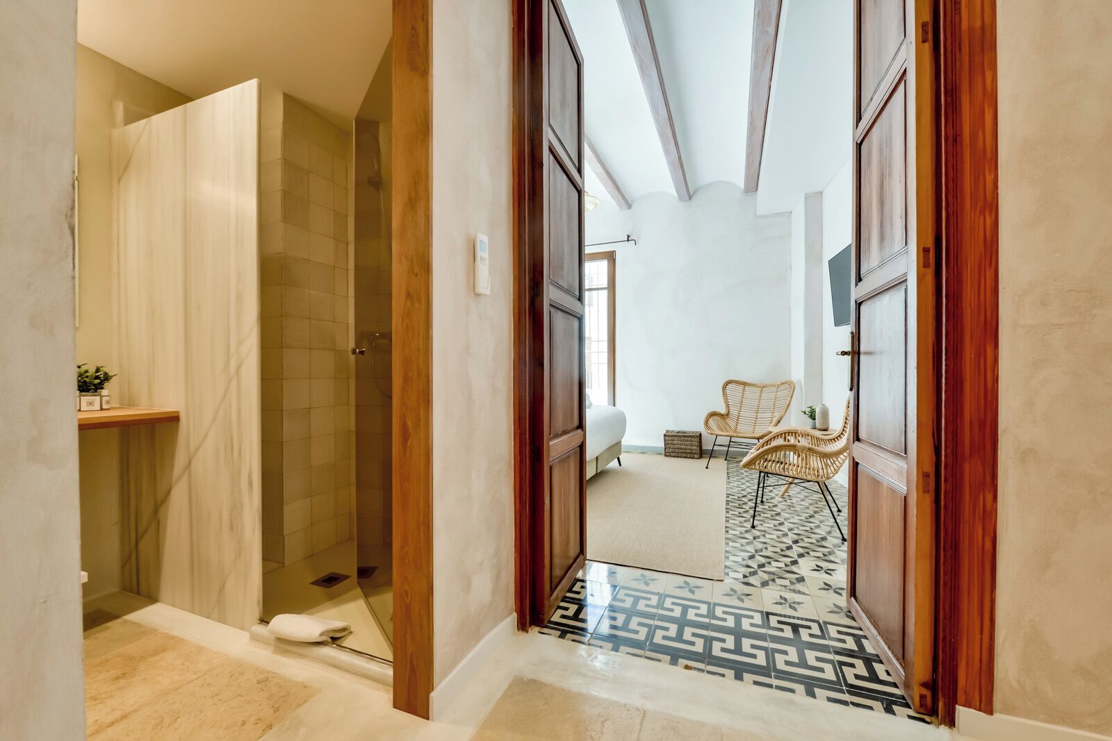 Un pasillo que conduce a un dormitorio con una cama, una silla de mimbre y una mesita.