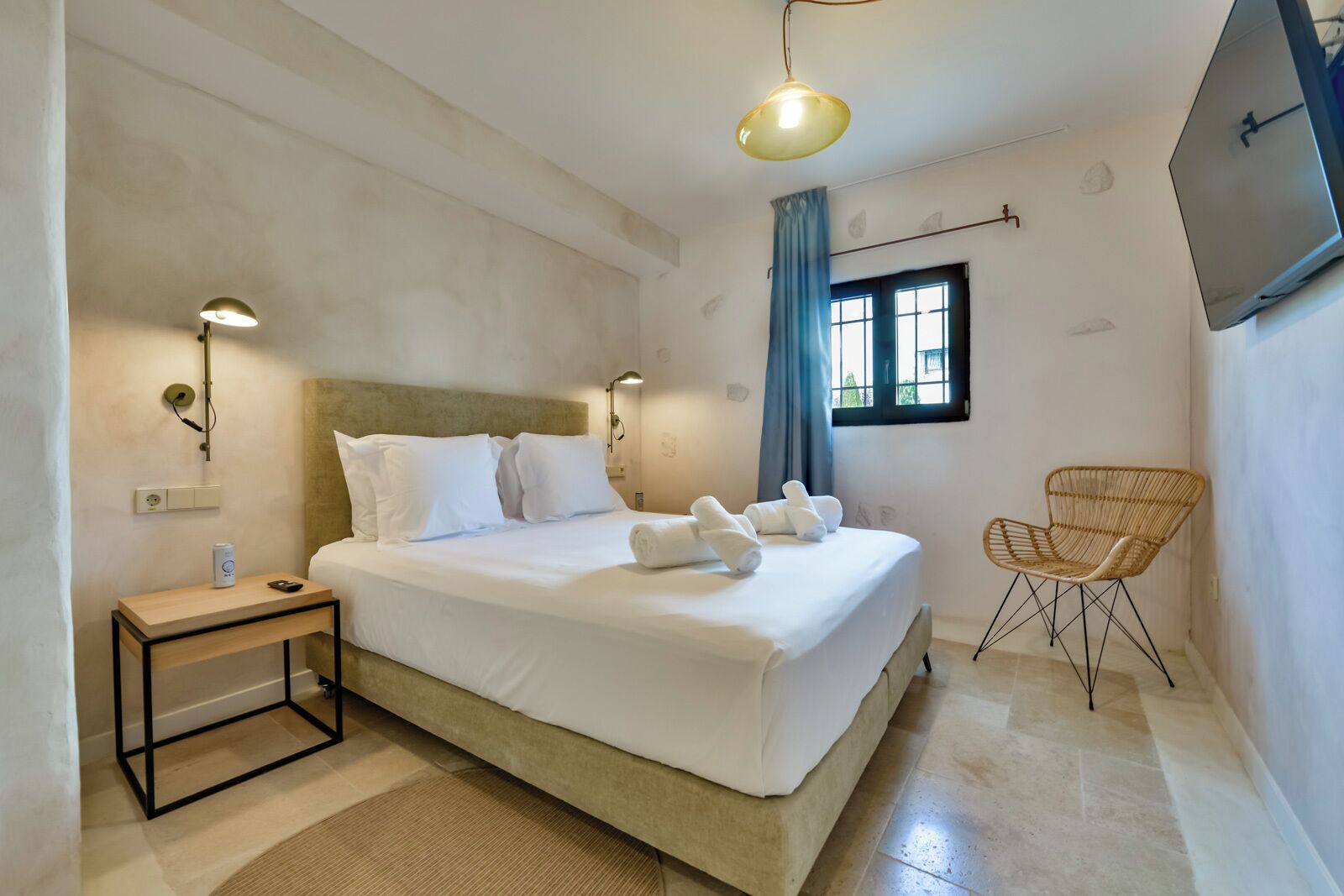 A bedroom with a bed, bedside table, lamp, chair, and a window with curtains.