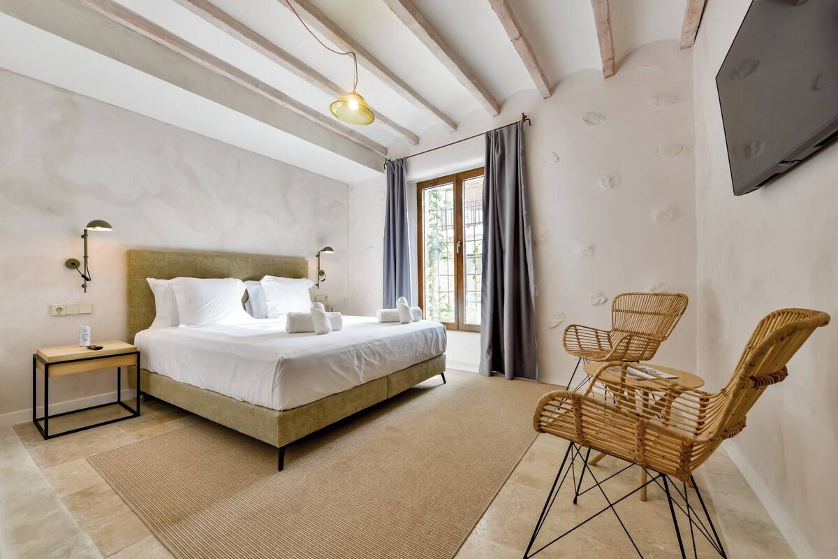 Une chambre à coucher avec un lit, des tables de chevet, un téléviseur fixé au mur et une fenêtre avec des rideaux.