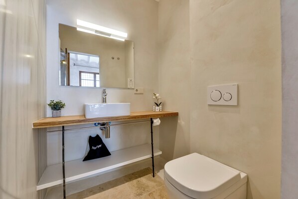 A modern bathroom with a white sink, mirror, and toilet. There is a towel rack and a small plant on the counter.