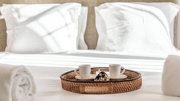 A neatly made bed with white linens, a tray with two cups and a small decorative item, and rolled towels on the bed.