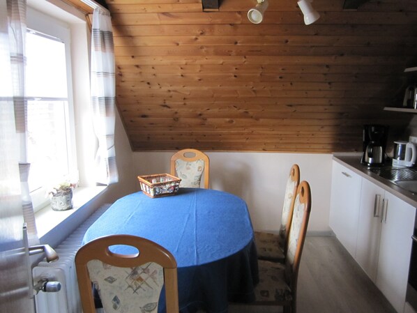 A cozy kitchen with wooden ceiling, a dining table with a blue tablecloth, and chairs.