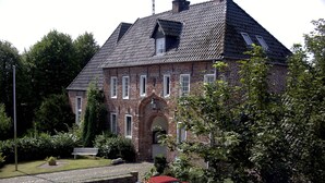 Um edifício de tijolos com telhado íngreme, várias janelas e uma entrada central com arco.