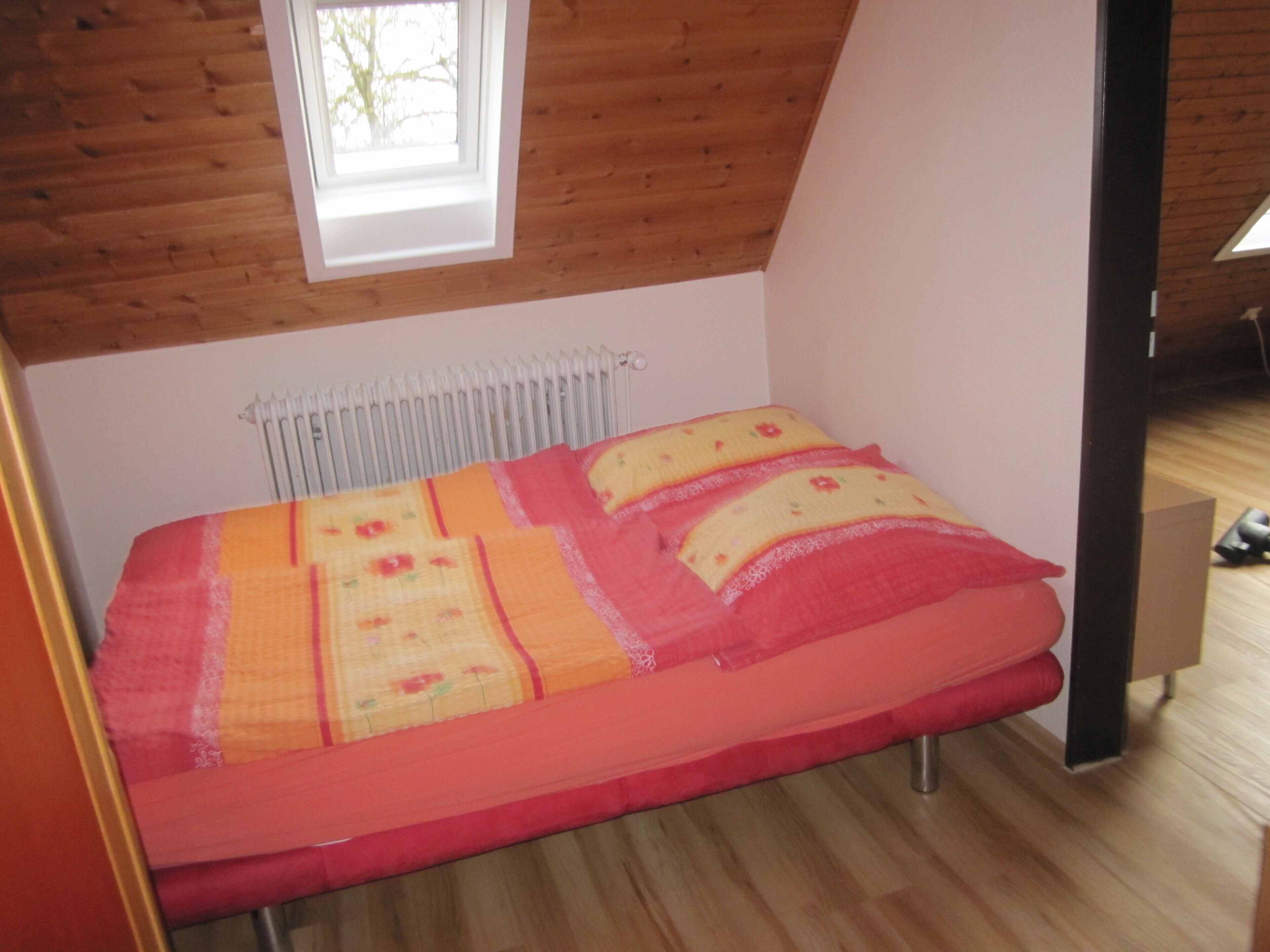 Et lille, hyggeligt soveværelse med træloft, en radiator og en seng med et farverigt tæppe.