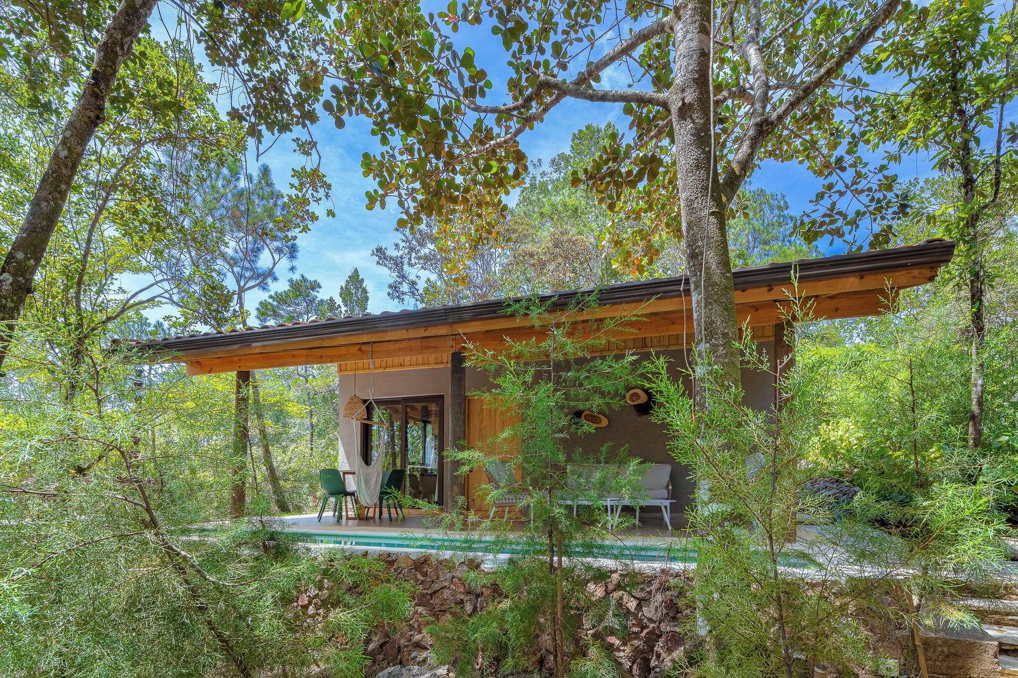 Una casa moderna con terraza de madera, rodeada de árboles y una piscina.