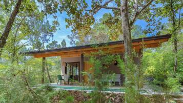 Una casa moderna con terraza de madera, rodeada de árboles y una piscina.