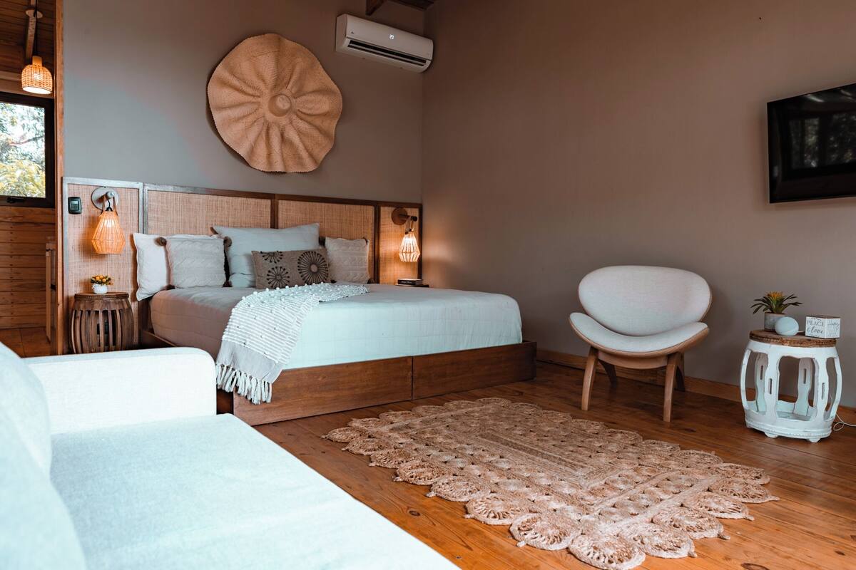 A bedroom with a wooden bed, a white chair, a round wall decoration, and a small table with a plant.