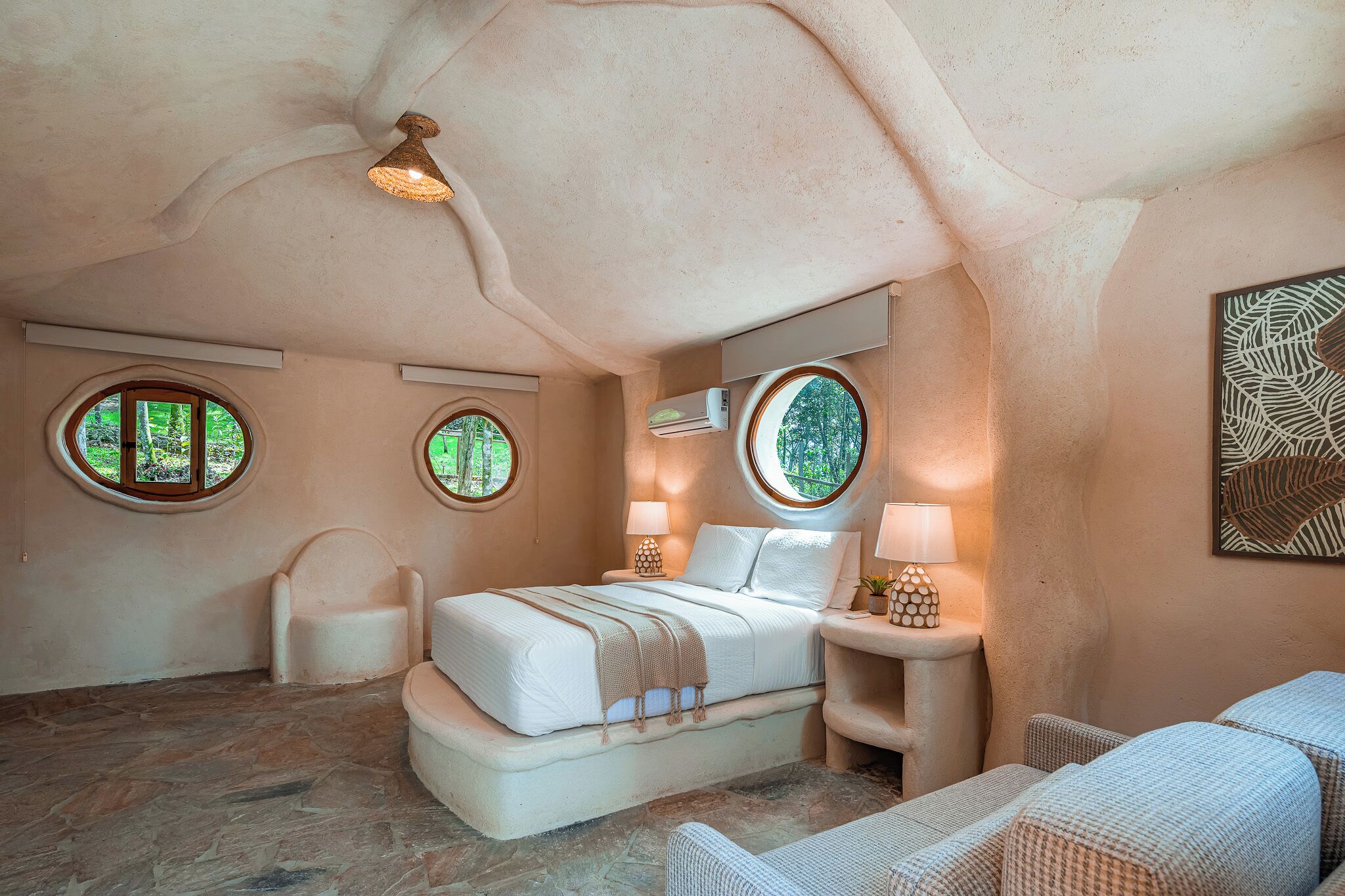 Een slaapkamer met een uniek architectonisch ontwerp, met een bed, twee stoelen en een klein tafeltje met lampen.