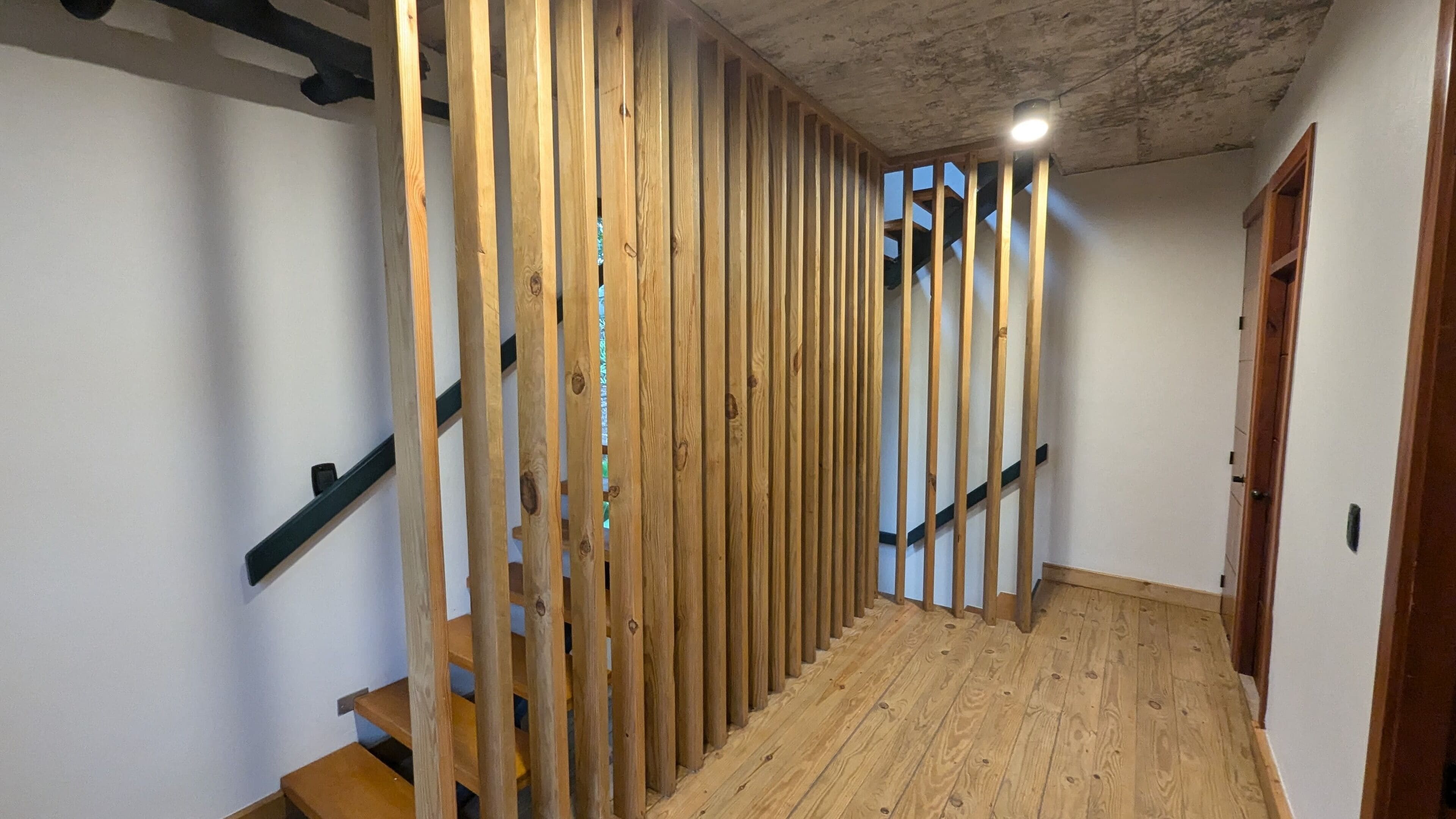 A wooden staircase with a modern design, leading to a room with a white wall and a visible door.