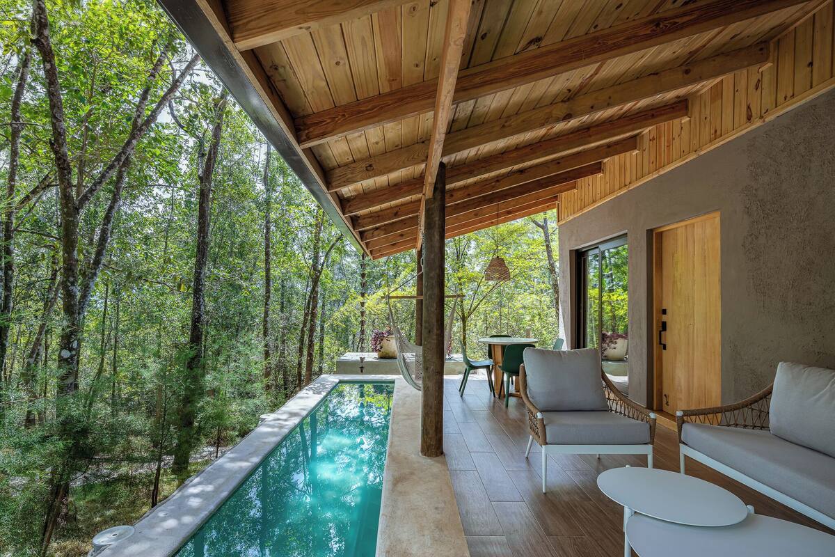 A modern outdoor pool area with wooden beams, a sofa, and a table.
