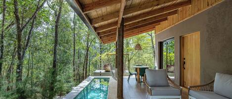 A modern outdoor pool area with wooden beams, a sofa, and a table.