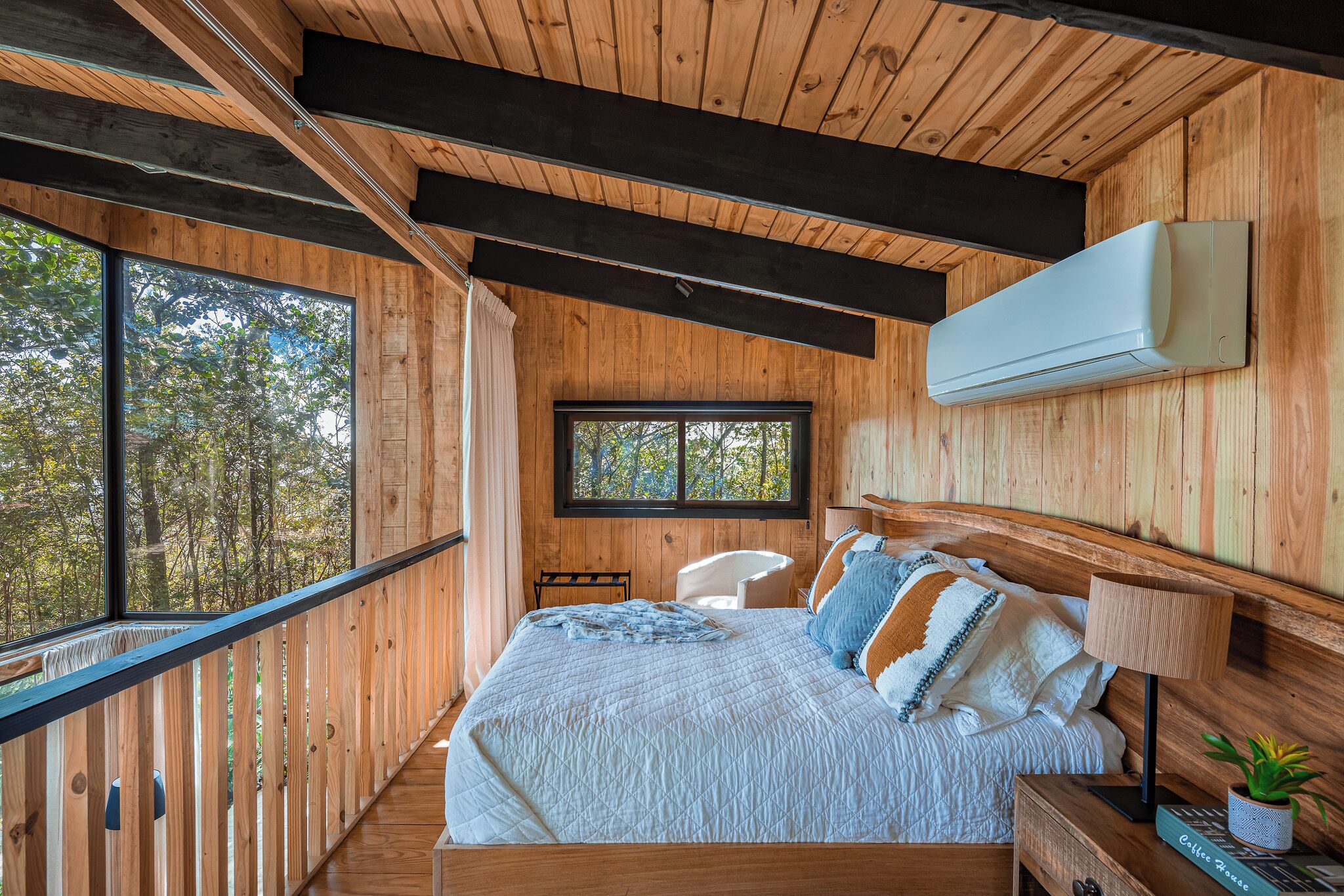 A wooden cabin bedroom with a large bed, a window, and a mounted air conditioner.