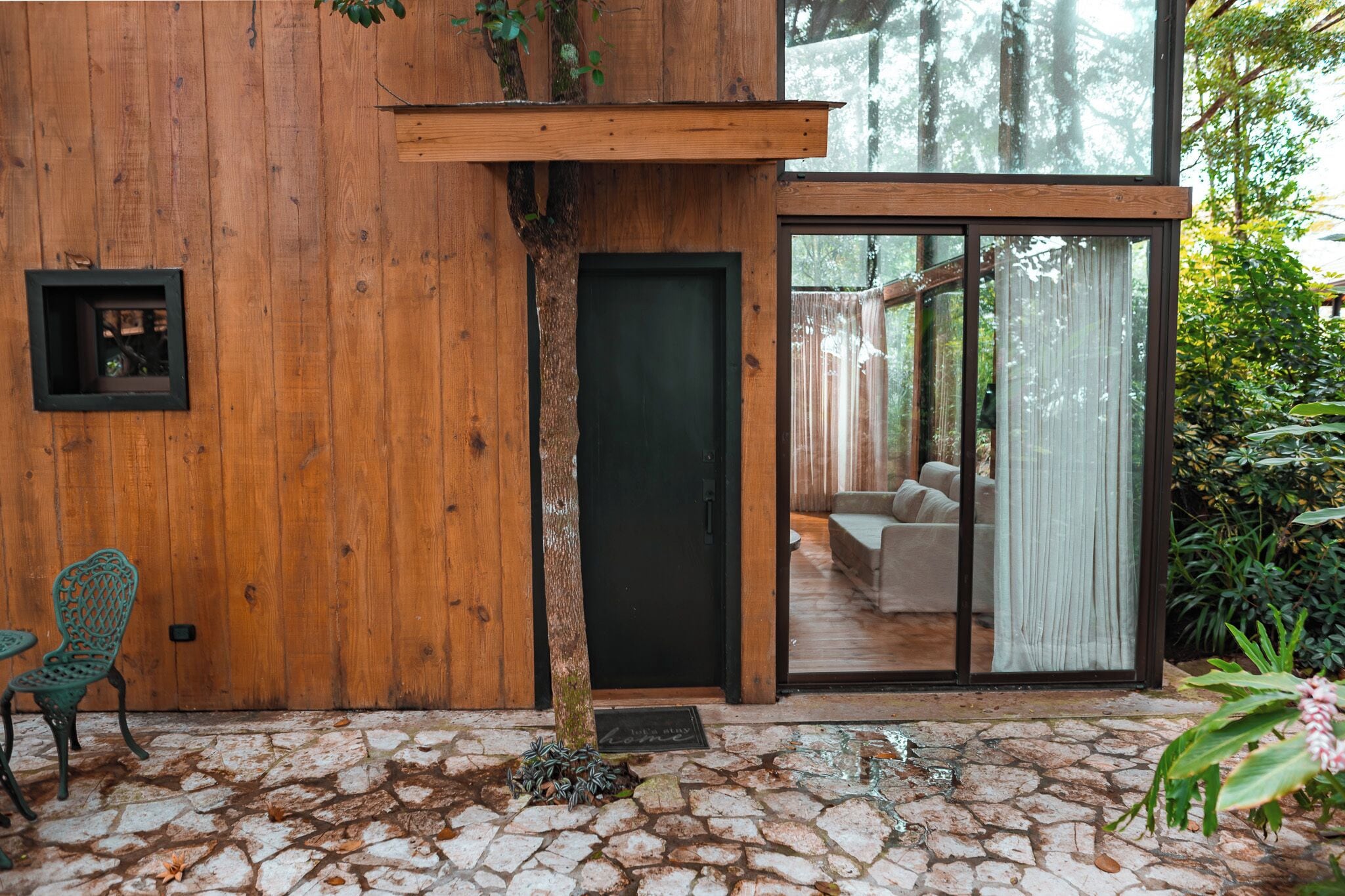 Fachada de madera con puerta de vidrio y un patio empedrado de piedra.