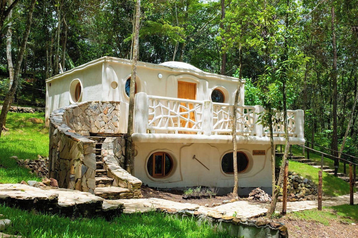 A treehouse with a stone staircase, a wooden door, and a balcony with a white railing.