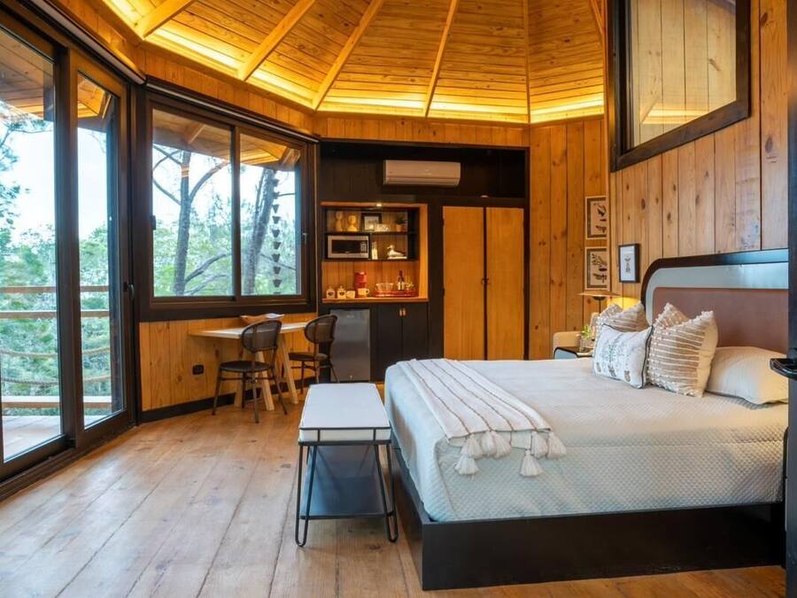 Un dormitorio con techo de madera, una cama, un escritorio y vistas al exterior.