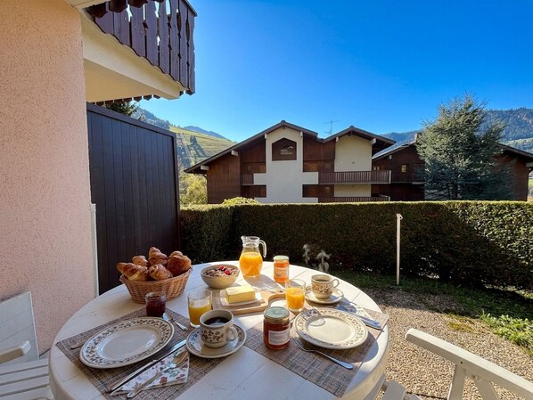 A breakfast table set outdoors with croissants, fruit, juice, and coffee.