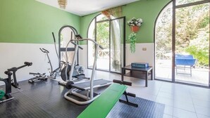 A gym with exercise equipment, a bench, and a view of the outdoors through large windows.