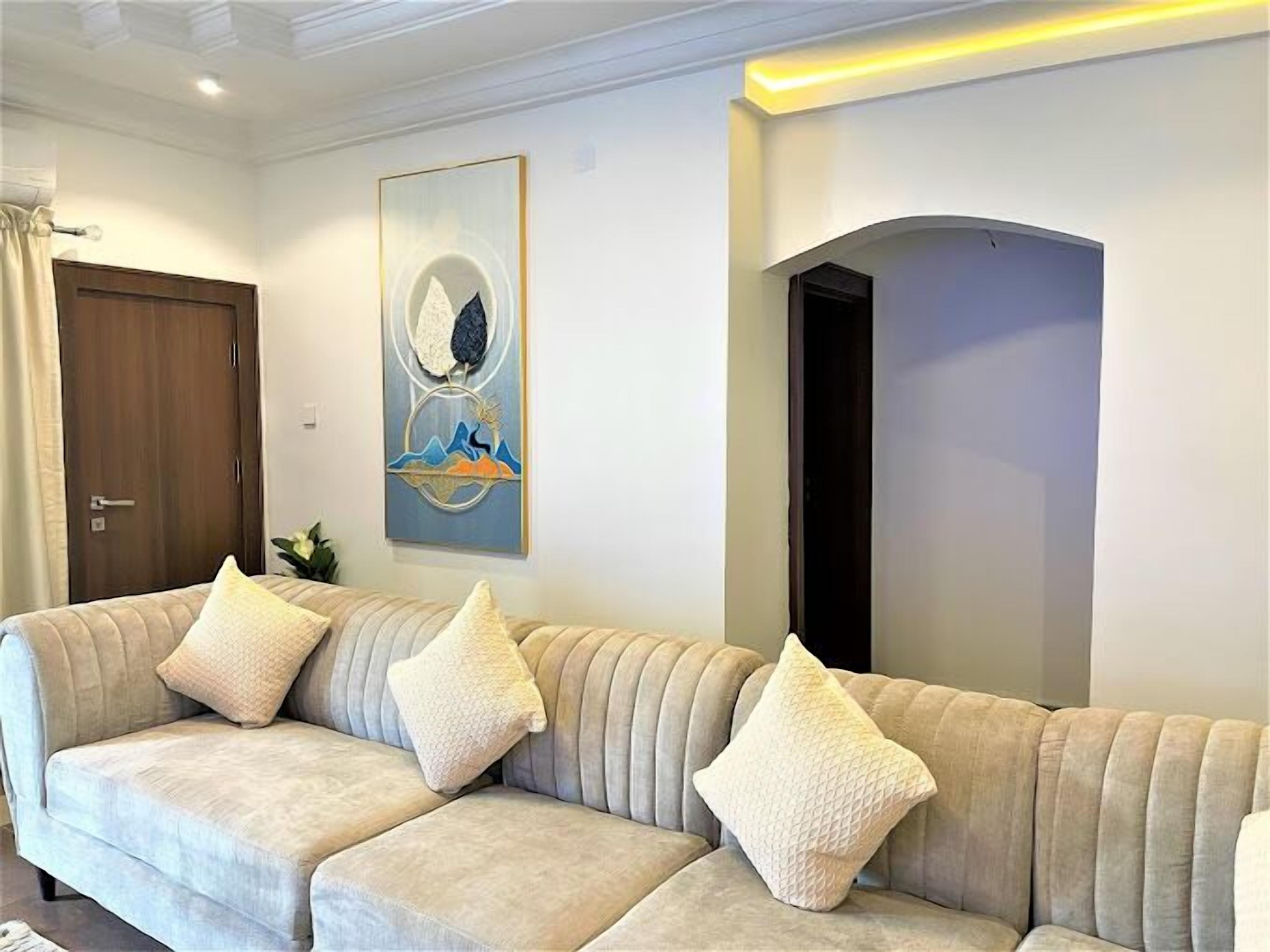 A living room with a beige sofa, three cushions, a painting, and a wooden door.