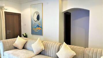 A living room with a beige sofa, three cushions, a painting, and a wooden door.