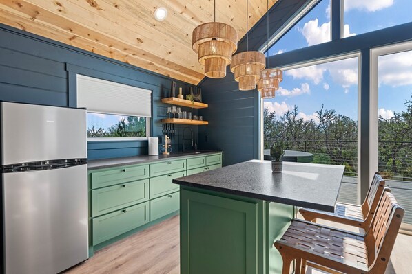 A modern kitchen with green cabinets, a stainless steel refrigerator, and a large window overlooking greenery.