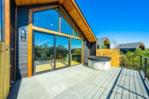 A modern wooden cabin with large glass doors, a deck, and a hot tub. - Chin 1 (Fredericksburg)