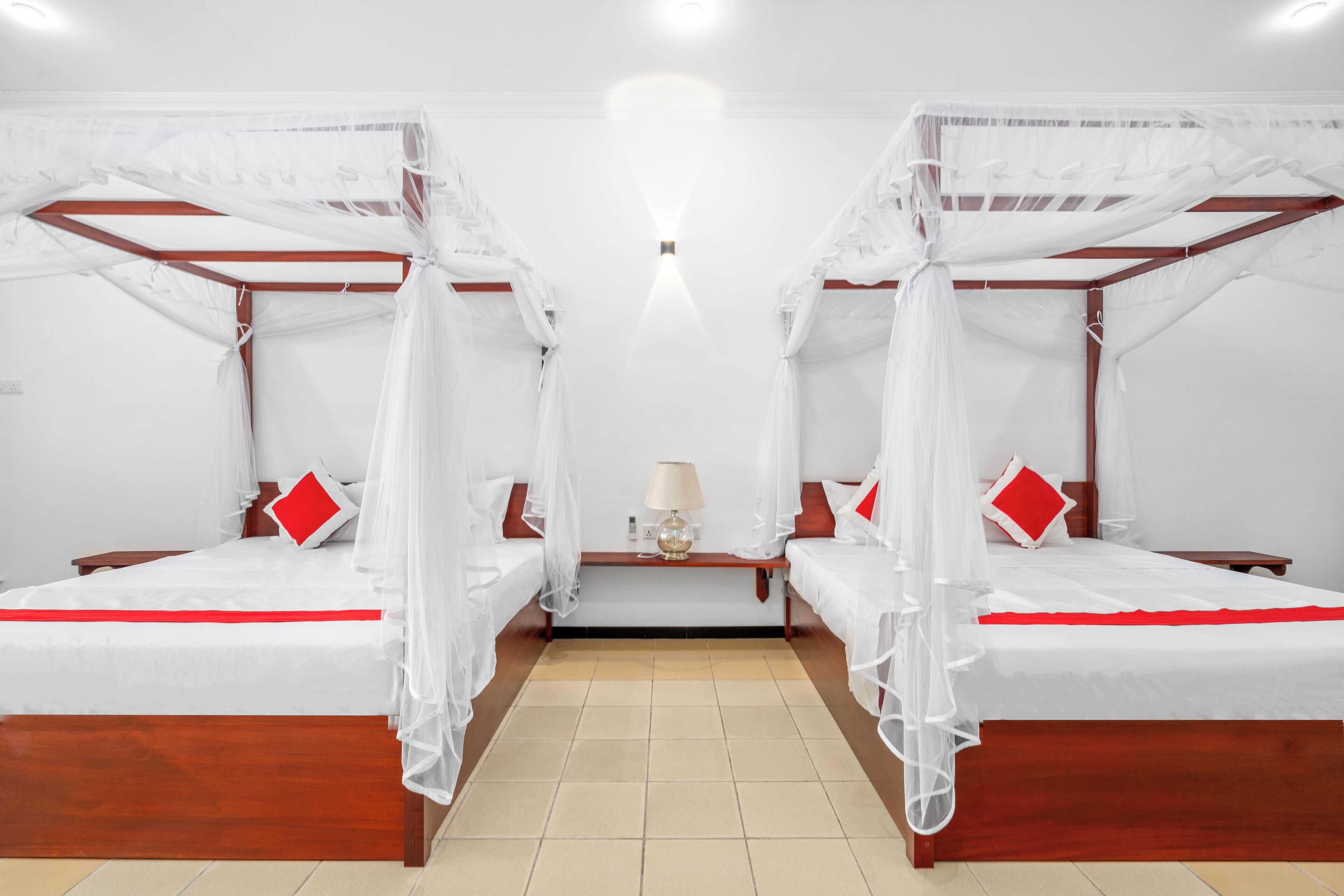 A room with two beds, each with a canopy, a nightstand, a lamp, and a red pillow.