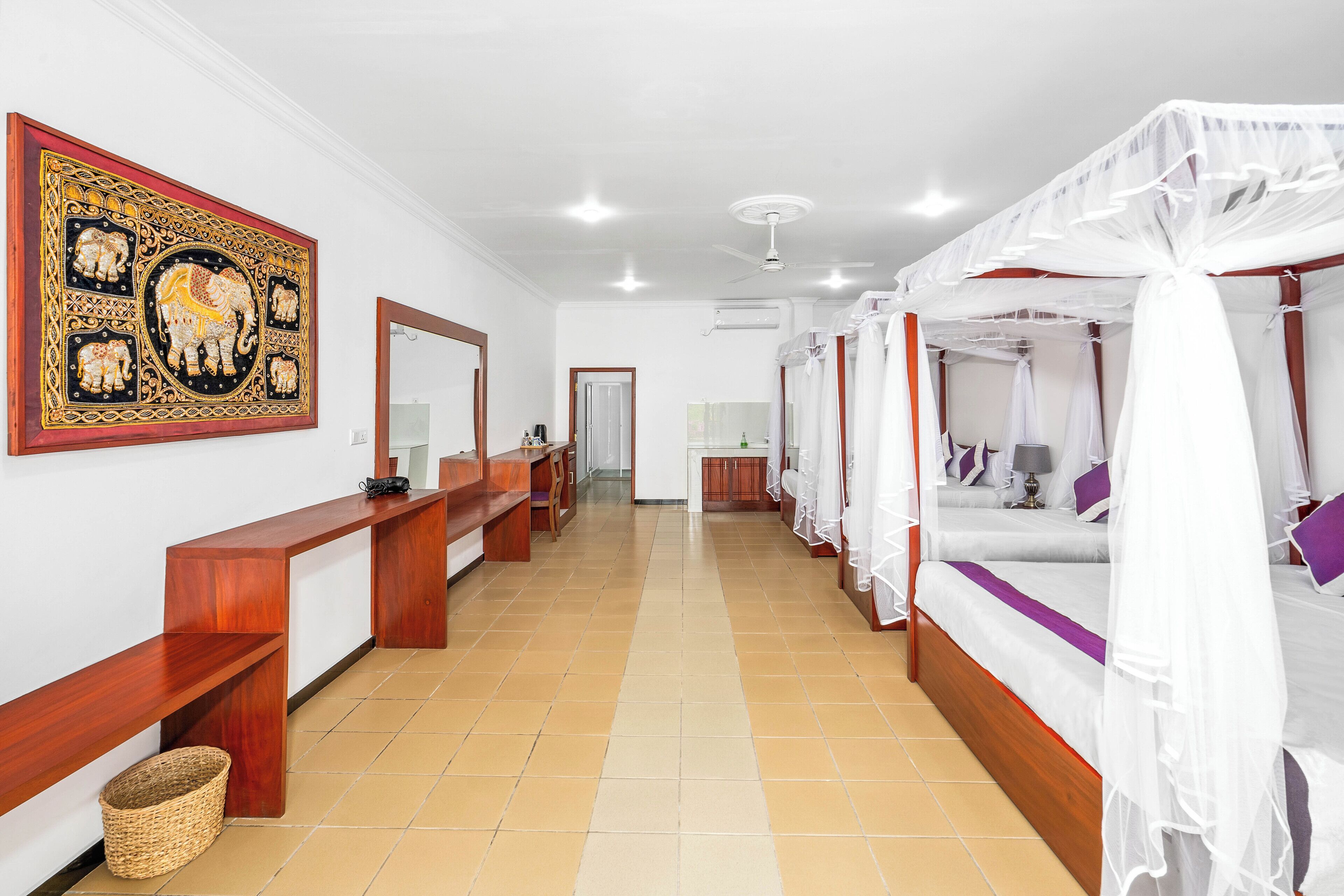 A hotel room with a large elephant painting, a wooden bench, a bed with a canopy, and a tiled floor.