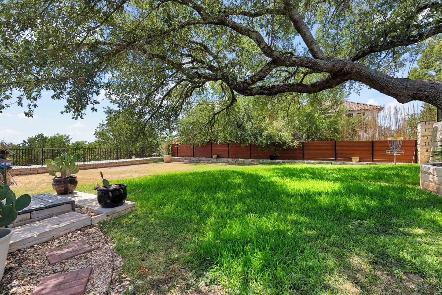 A well-maintained backyard with a grassy lawn, a large tree, and a wooden fence.